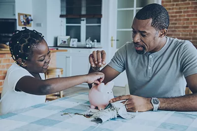 Dad and daughter putting money into a piggy bank